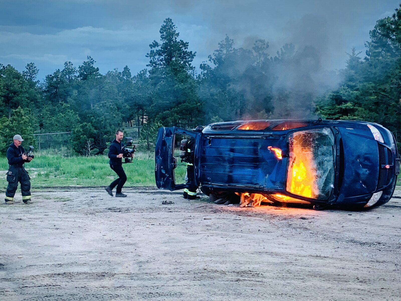 Camera crew filming a staged vehicle fire stunt in the field, behind the scenes of Mind Shift film production