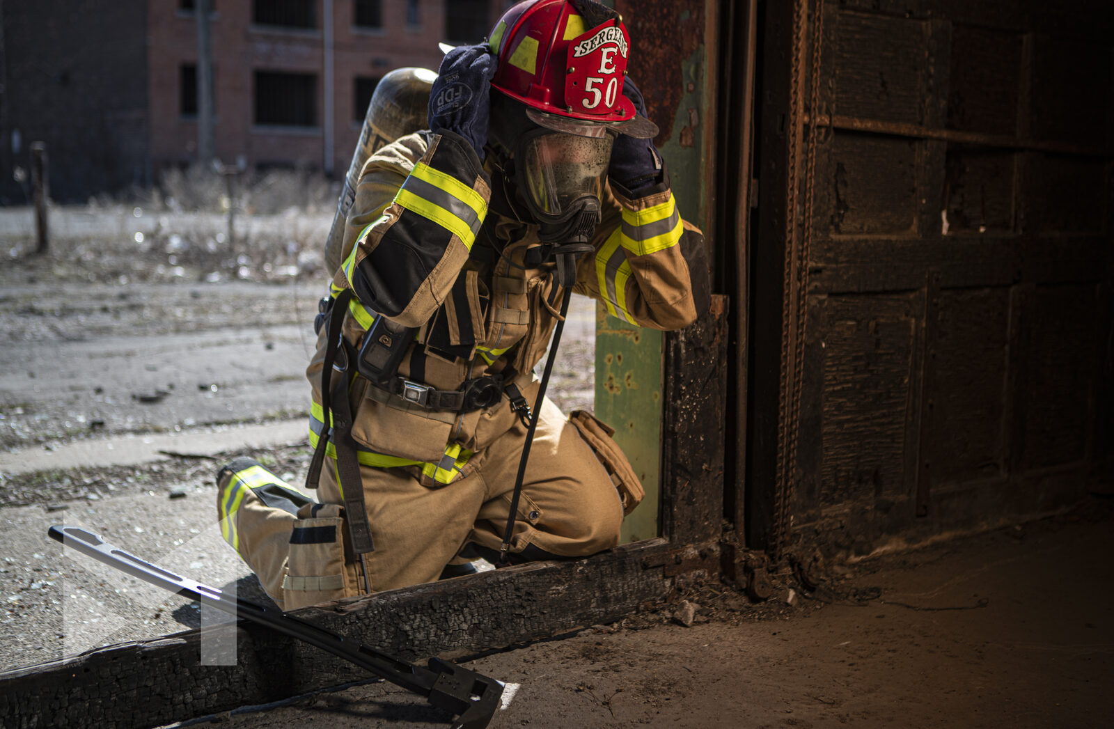 Firefighter in a red helmet working a charred metal door during rescue training, fire service photography by Mind Shift
