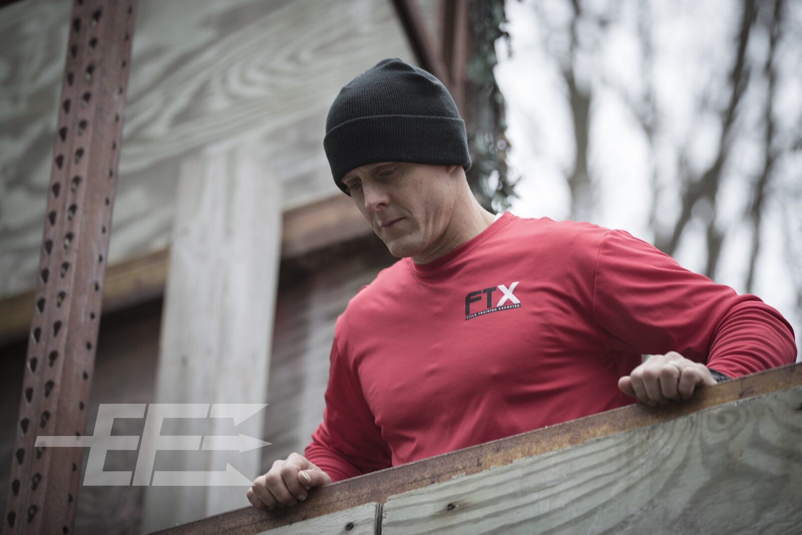 Trainee in an FTX training shirt leans on a wooden barricade at an outdoor Echelon Front field training exercise, tactical photography by Mind Shift